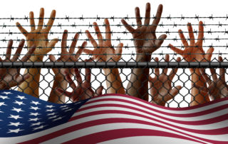 hands reaching over a barbed wire fence near an american flag